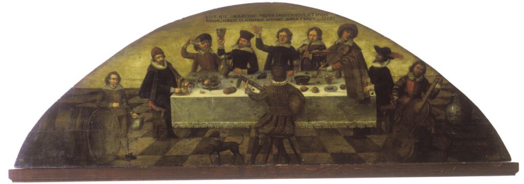 Historisches Wandgemälde mit der Szene "Fast mit den Studenten": einer festlichen Tafelrunde mit mehreren Männern in frühneuzeitlicher Kleidung; einige trinken Wein, andere musizieren, ein Pudel steht im Vordergrund.