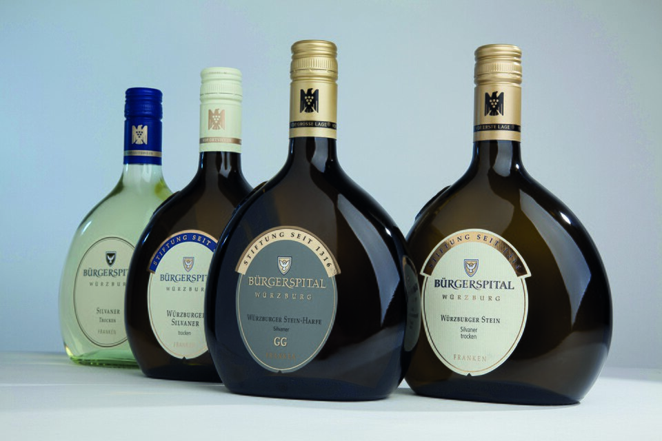 Vier Bürgerspital-Weine in Bocksbeutel-Flaschen vor einfarbiger Wand